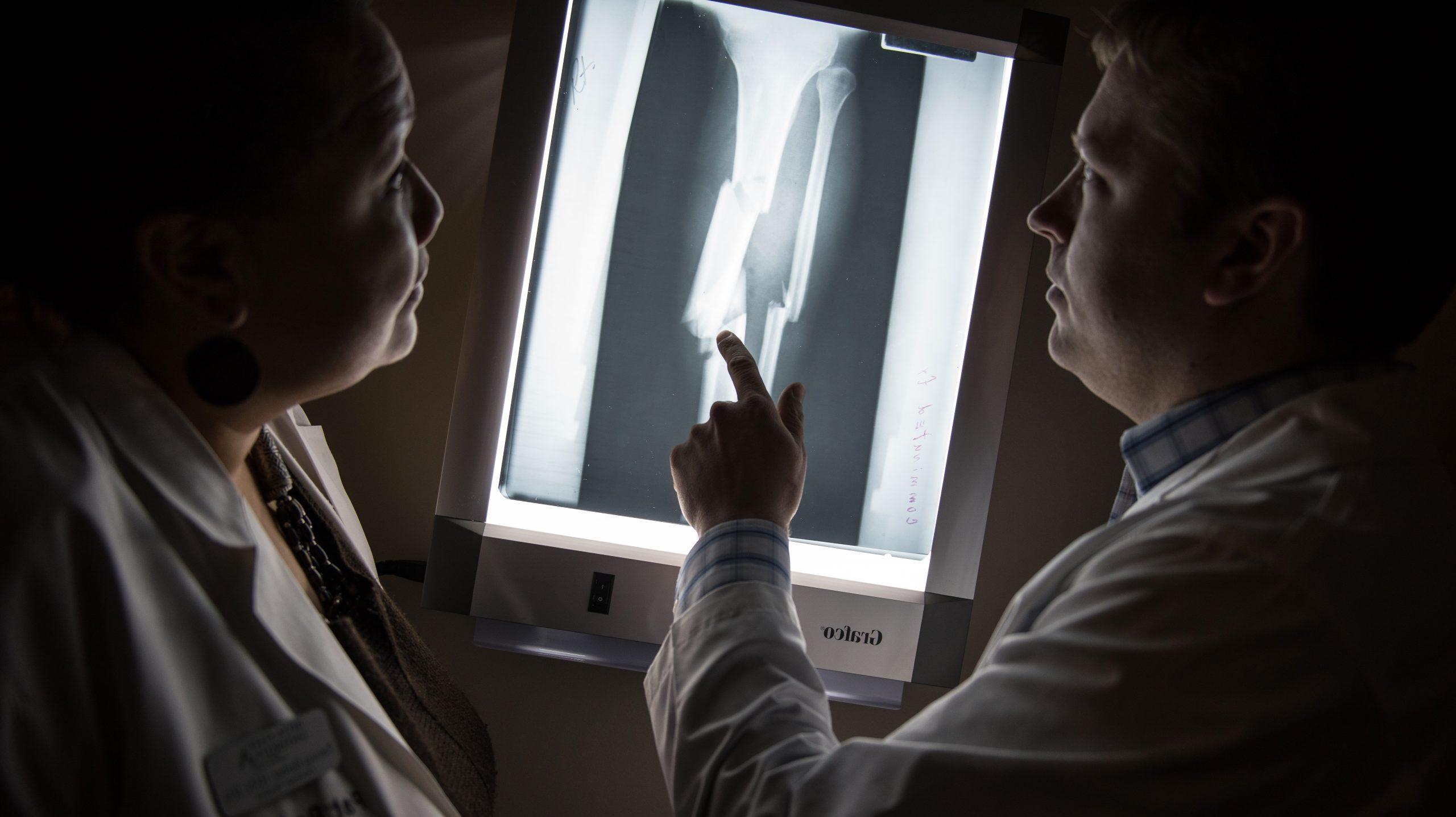Two nursing students interpreting x-ray of broken bone in a dark room.
