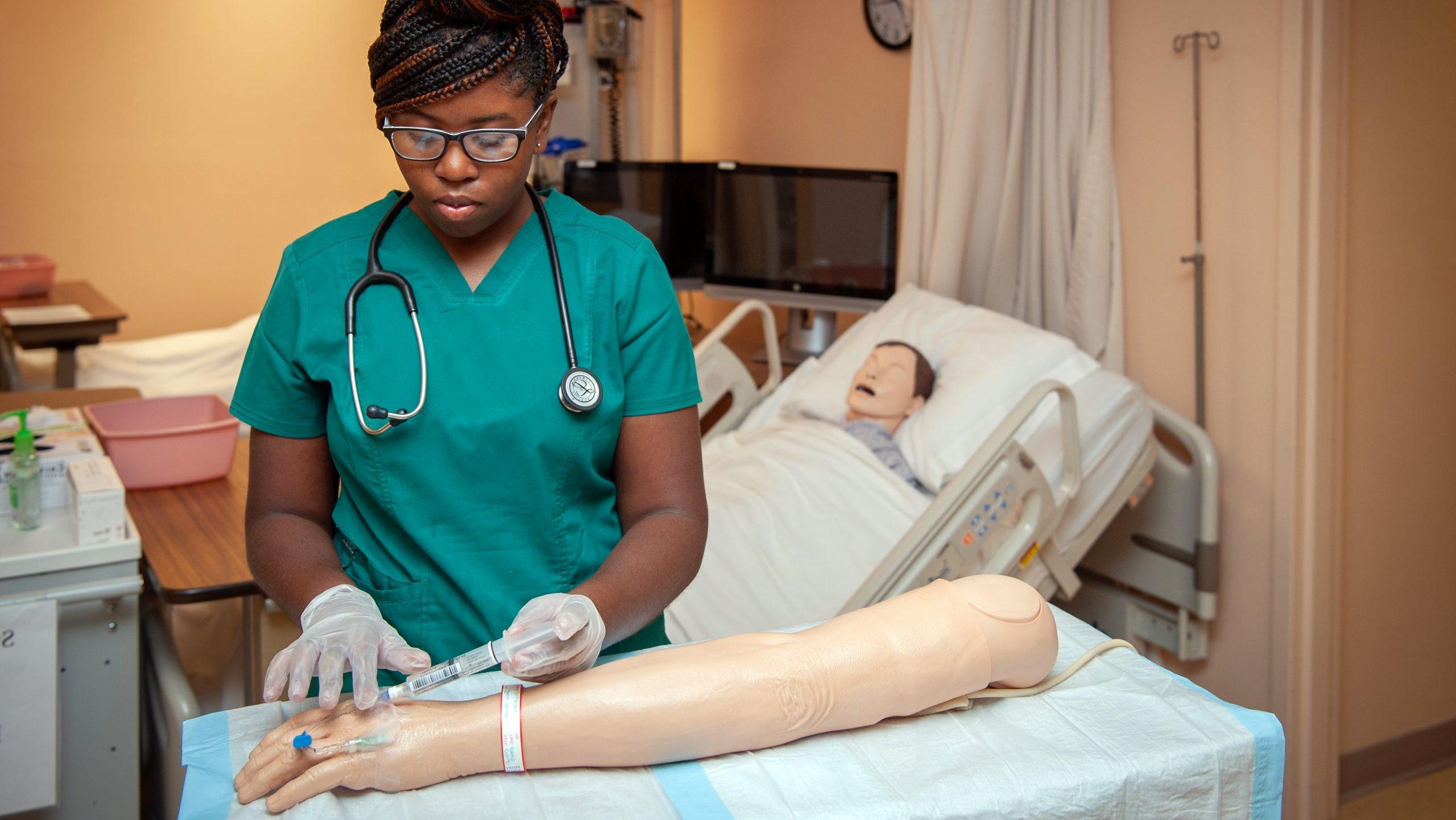 女学生在护理模拟实验室使用注射器和管在假人手臂上.